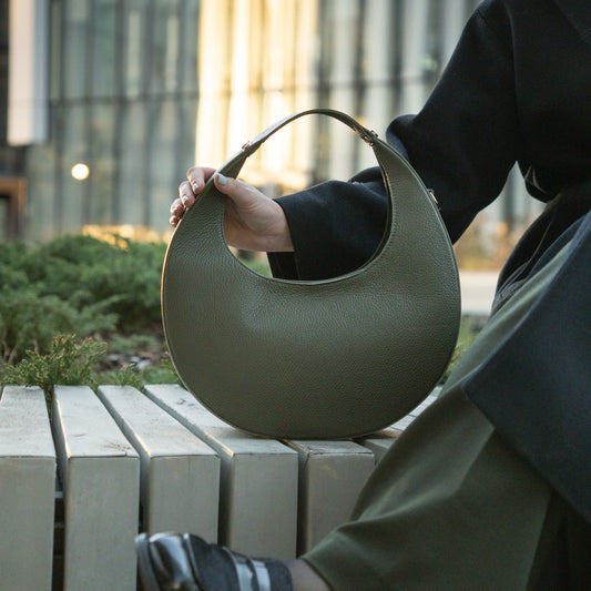 Person holding a green handbag outdoors with a blurred background