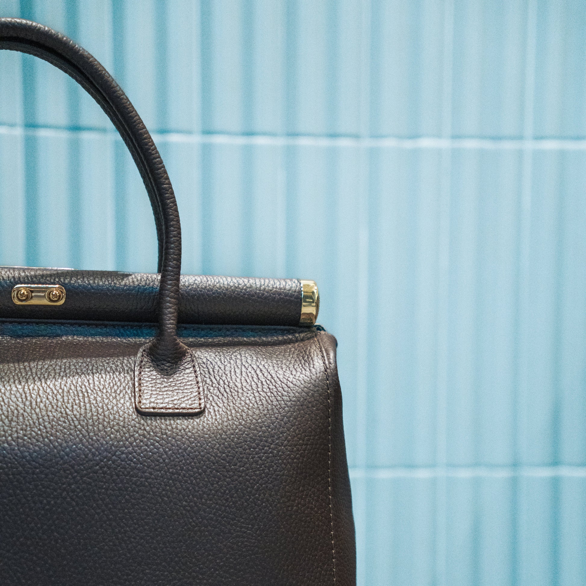 Brown leather handbag with gold clasp against a blue tiled wall