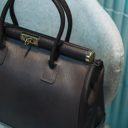 Brown leather handbag with gold clasp on a light blue background