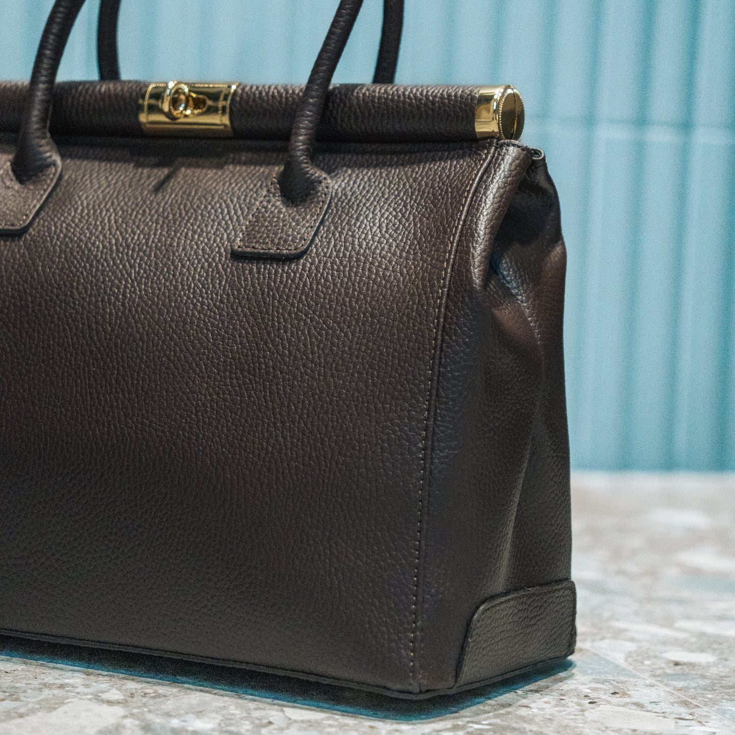Brown leather handbag with gold clasp on a textured surface