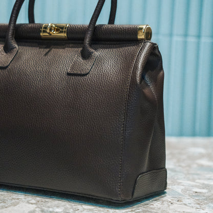 Brown leather handbag with gold clasp on a textured surface